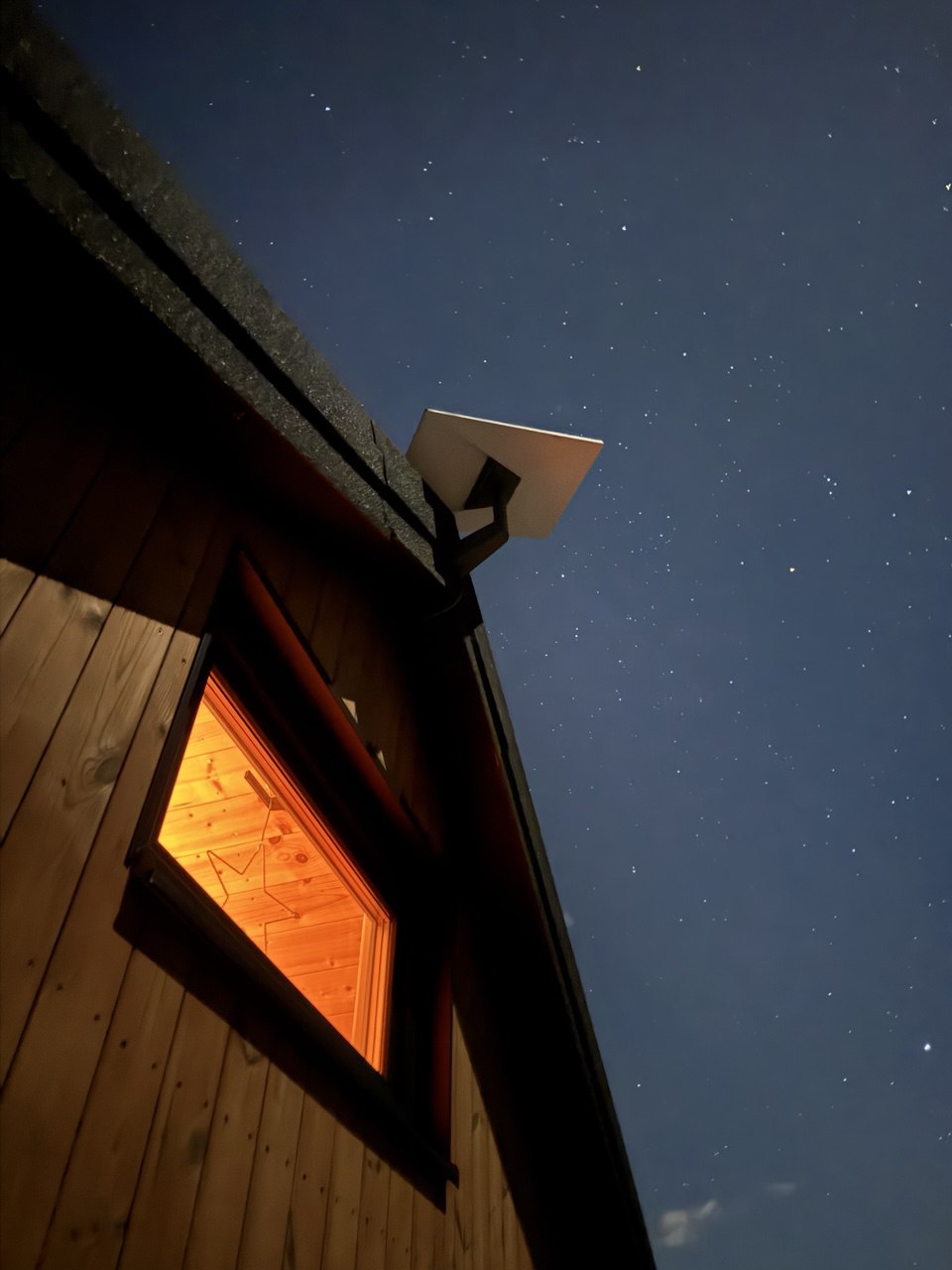 Starlink antena postavljena na krovu kućice pod zvjezdanim nebom